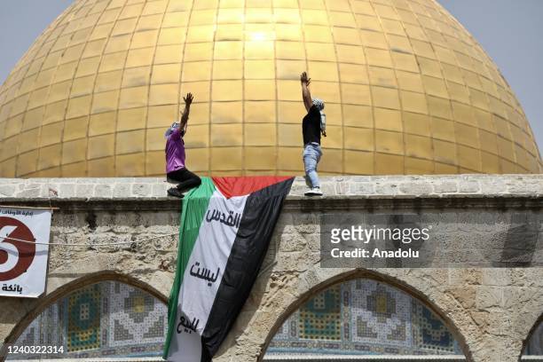 Two Palestinians hang a Palestinian flag on the walls of Al- Aqsa as Muslims gather to perform the last Friday prayer of holy fasting month of...