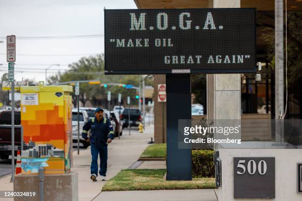 An oilfield worker walks past a sign that reads "M.O.G.A 'Make Oil Great Again'" in downtown Midland, Texas, U.S. On Monday, April 4, 2022. West...
