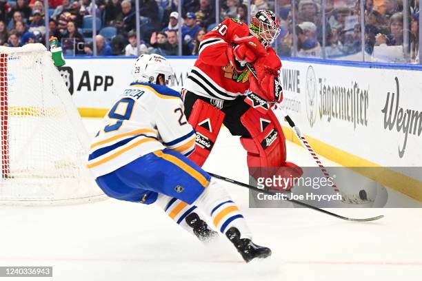 Collin Delia of the Chicago Blackhawks plays the puck from behind the net as Vinnie Hinostroza of the Buffalo Sabres defends during an NHL game on...