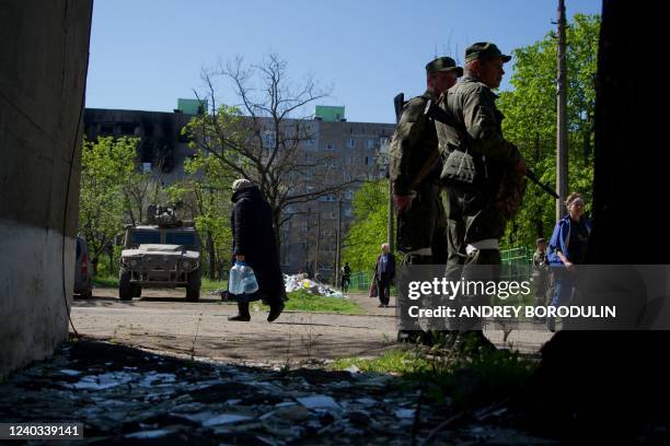 Residents walk in the city of Mariupol as the self-proclaimed Donetsk People's Republic servicemen guard an area on April 29 amid the ongoing Russian...