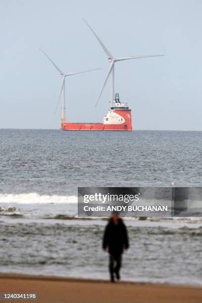 Man walks on the beach with wind turbines on the background, off the coast of Aberdeen, in the North East of Scotland, on April 29, 2022.