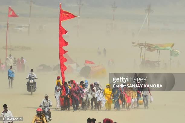 People carrying a religious flag walk along the banks of Sangam, the confluence of the rivers Ganges, Yamuna and mythical Saraswati, on a summer...