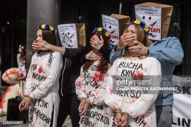 Ukrainian activists wearing dresses with the names of Ukrainian cities destroyed by Russians and bloodstains take part in a demonstration in front of...