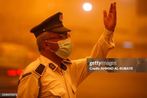 An Iraqi policeman directs traffic during a severe dust storm in the capital Baghdad on May 1, 2022. - Flights were grounded today due to poor...