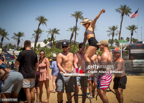 Girl surfs the table as country music fans play drinking games where a table is moved down the line amid high heat while camping in the RV Resort...
