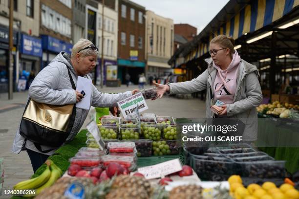 Shoppers make purchases at a market stall in Dudley town centre in central England on April 29, 2022. - Rampant inflation and lockdown-breaking...