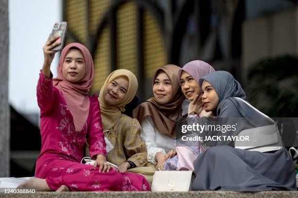 Young women take pictures following morning prayers at The Foundation of the Islamic Centre of Thailand mosque during Eid al-Fitr celebrations,...