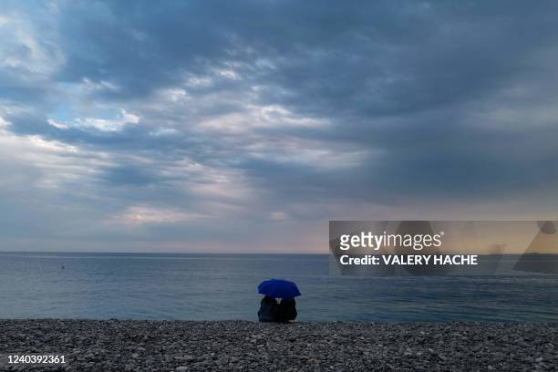 Two people sit in front of Mediterranean sea along the "Promenade des anglais" on the French riviera city of Nice, on May 01, 2022.