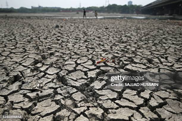 People walk across a patch of parched riverbed of Yamuna on a hot summer day in New Delhi on May 2, 2022. -