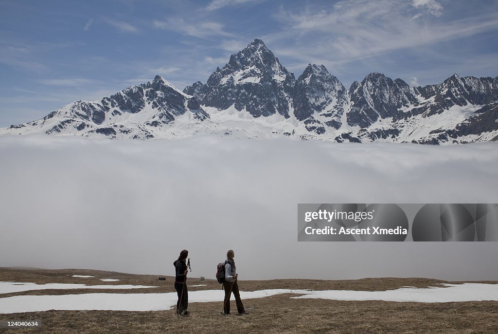 Hikers look back at snowy mtns rising above fog