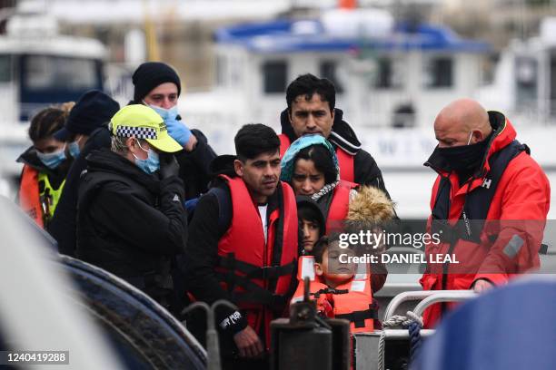 Migrants, picked up at sea while attempting to cross the English Channel, are helped by a member of the UK Border Force to disembark from a boat, in...