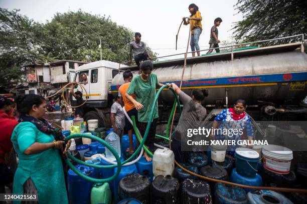 Residents use hoses to collect drinking water from a tanker truck during a hot summer day in New Delhi on May 3, 2022.