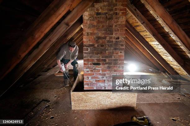 In the attic of a home in Woolwich, John Mickles applies spray foam to the base of a box used as an air gap around a chimney so that insulation he...