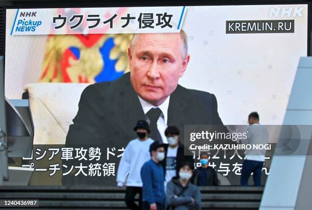 Pedestrians walk past a screen displaying Russian President Vladimir Putin during a news broadcast about Russia's invasion of Ukraine, in the...