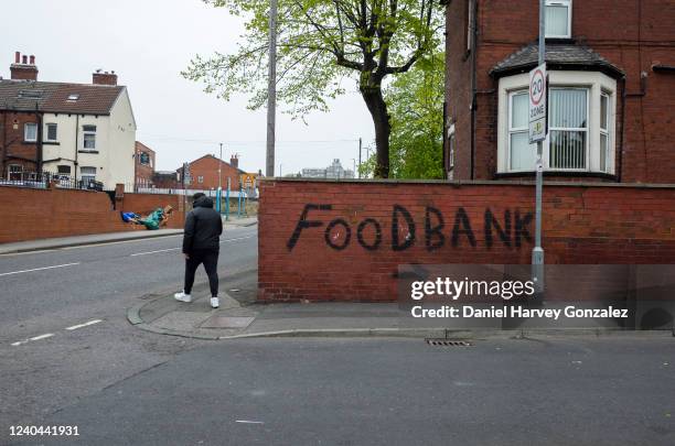 Man wearing a hooded jacket passes by bold, black graffiti that points towards a local food bank in Harehills, one of the most deprived areas of...