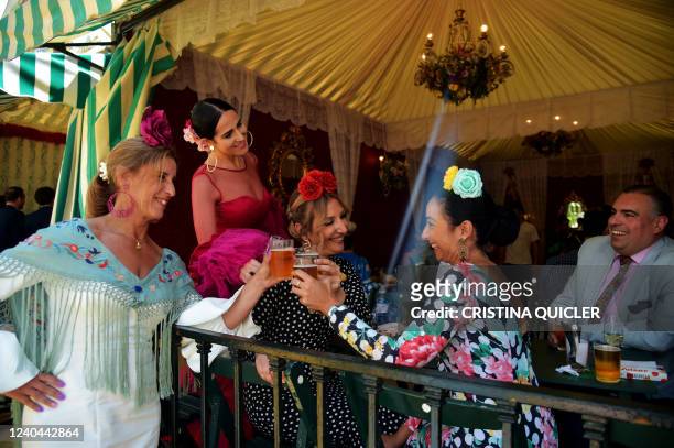 People in typical Sevillian costumes drink a toast at a 'caseta' during the 'Feria de Abril' festival in Seville on May 4, 2022.