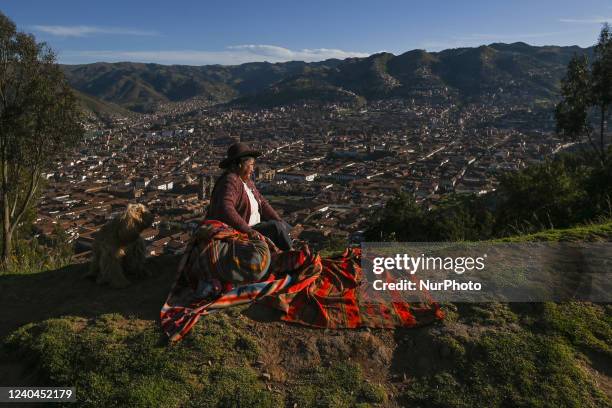 Traditionally dressed Quechua woman seats near the road with the panorama of Cusco town in the background, close to the statue of Christ. On Sunday,...