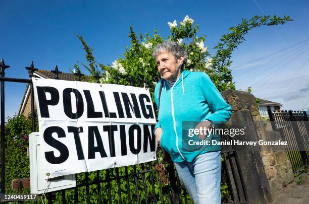 In sunny weather, a woman makes her way past a sign indicating the location of a local polling station as voters head to polling stations to cast...