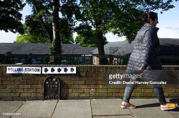 Woman makes her way past a sign with arrows that indicate the direction towards a local polling station as voters head to polling stations to cast...