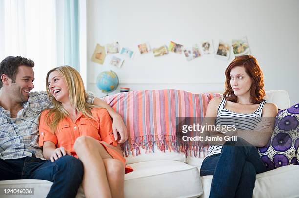 annoyed friend next to romantic couple on couch - jealousy stockfoto's en -beelden