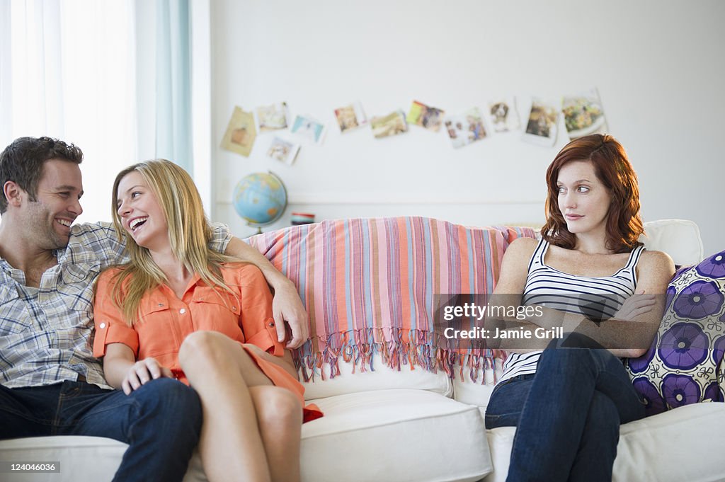 Annoyed friend next to romantic couple on couch
