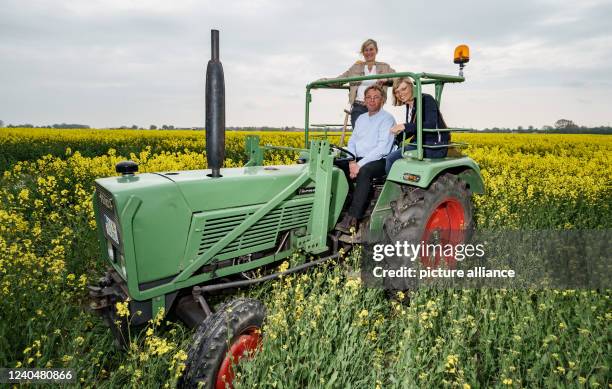 May 2022, Schleswig-Holstein, Norddeich: Maike and Carsten Witthohn, rapeseed farmers and millers, sit on a tractor in a rapeseed field together with...