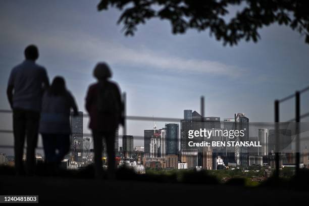 People look out over London's secondary central business district of Canary Wharf in the spring sunshine from Greenwich Park on May 6, 2022. - The...