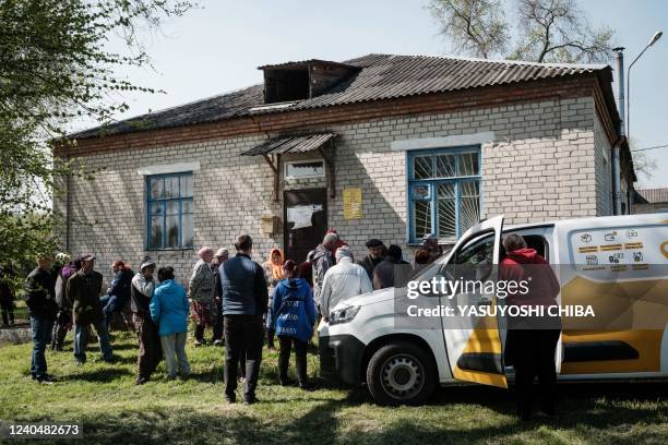 People gather in front of a closed post office to receive their pension from a postal delivery van that reached the frontline despite the ongoing...