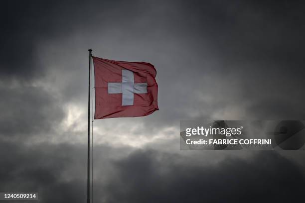 The Swiss national flag is seen floating under a cloudy sky in Geneva on May 5, 2022.