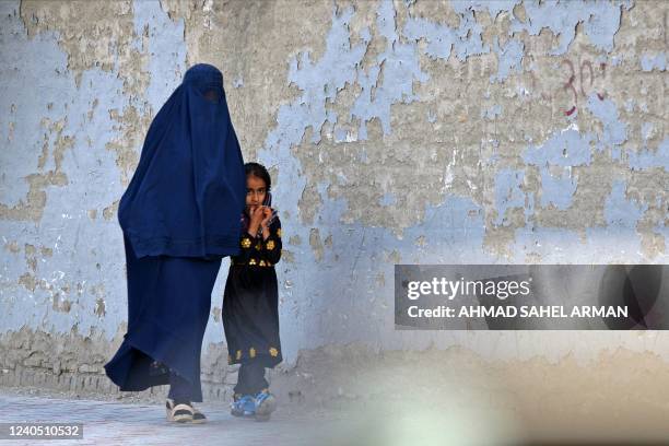 Burqa-clad woman walks with a girl along a street in Kabul on May 7, 2022. - The Taliban on May 7 imposed some of the harshest restrictions on...