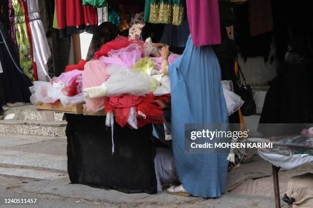 Burqa-clad woman browses through children garments at a shop in Herat on May 7, 2022. - The Taliban on May 7 imposed some of the harshest...