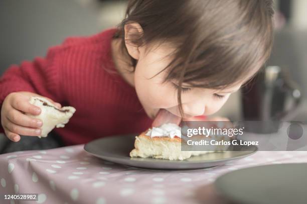 child wearing a red top licking the cream off a cake on a plate - human tongue surface stock pictures, royalty-free photos & images