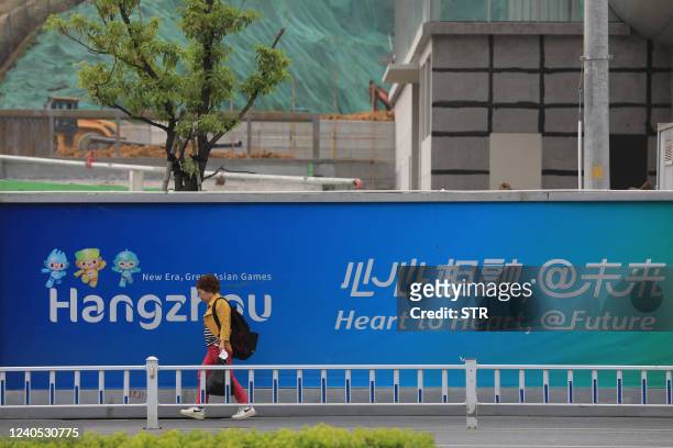 Resident walks past a wall with images of the 2022 Asian Games in Hangzhou, in China's eastern Zhejiang province on May 8, 2022. - China's ambitions...