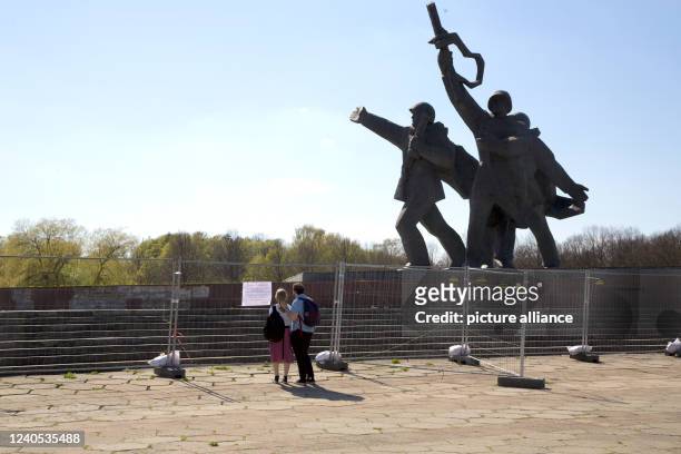May 2022, Latvia, Riga: A couple stands in front of the cordoned off part of the Victory Monument due to its technical condition. An exhibition of...