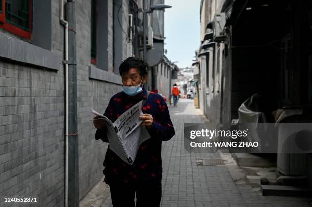 An elderly man reads a newspaper while walking in an alley in Beijing on May 9, 2022.