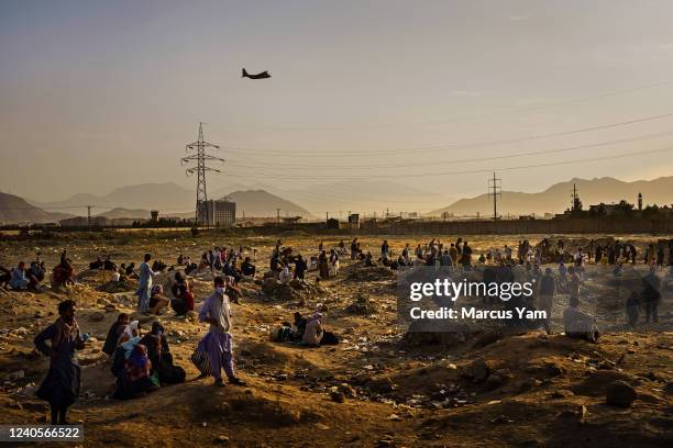 Military transport plane departs overhead as Afghans hoping to leave the country wait outside the Kabul airport on Aug. 23, 2021. Since the Taliban...