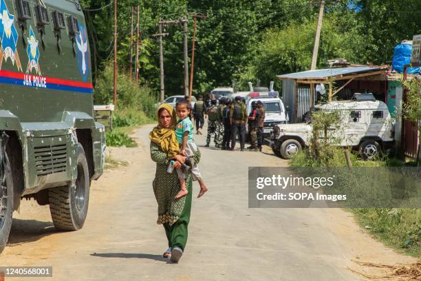 Kashmir woman carrying a child walks past Indian paramilitary troopers standing on guard at the site of an encounter which according to local media...