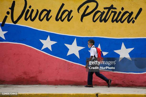 Boy walks in front of a mural that in Spanish says: Long live the homeland, by the west side of the city in Caracas, Venezuela on May 9, 2022.