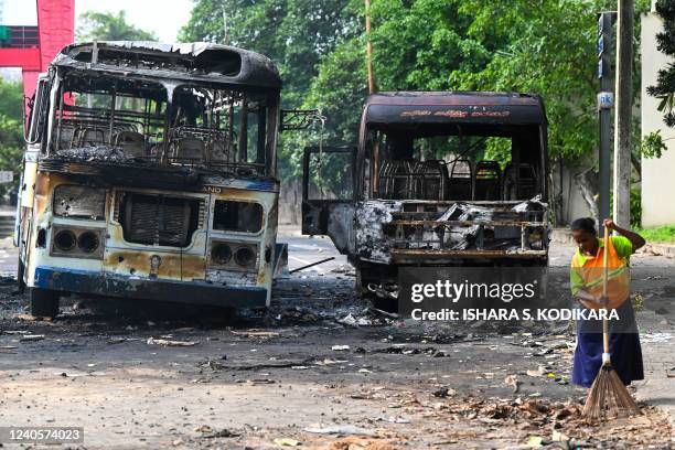 Worker sweeps the street alongside the burnt buses near Sri Lanka's former prime minister Mahinda Rajapaksa's official residence 'Temple Trees', a...