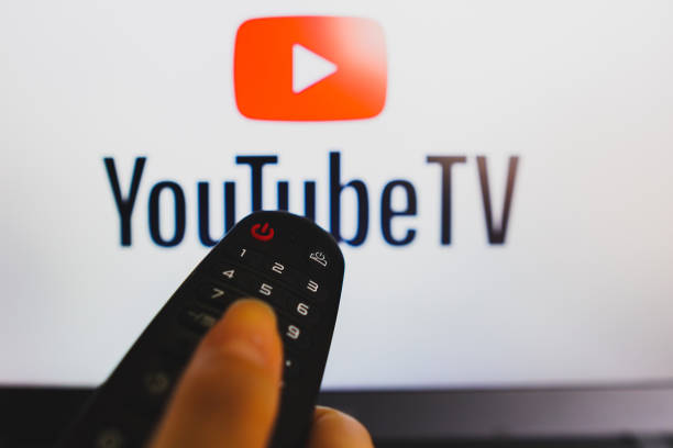In this photo illustration, a hand holding a TV remote control in front of a YouTube logo on a TV screen.