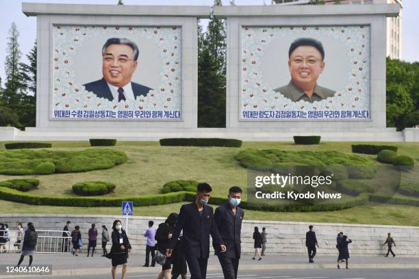 People wearing face masks walk by portraits of late North Korean leaders Kim Il Sung and Kim Jong Il in Pyongyang on May 6, 2022. North Korea's...