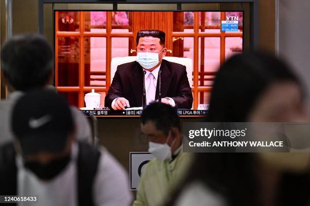 People sit near a screen showing a news broadcast at a train station in Seoul on May 12 of North Korea's leader Kim Jong Un appearing in a face mask...