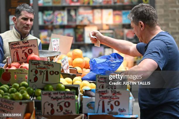 Customer pays for his fruit and vegetables with a ten pound sterling note, at a trader's market stall in London on May 12, 2022. - Britain's economy...