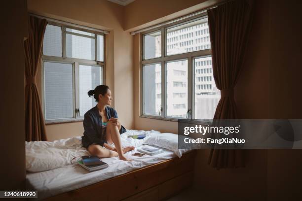 asian woman sit on bed looking though window in hong kong - hostel stock pictures, royalty-free photos & images