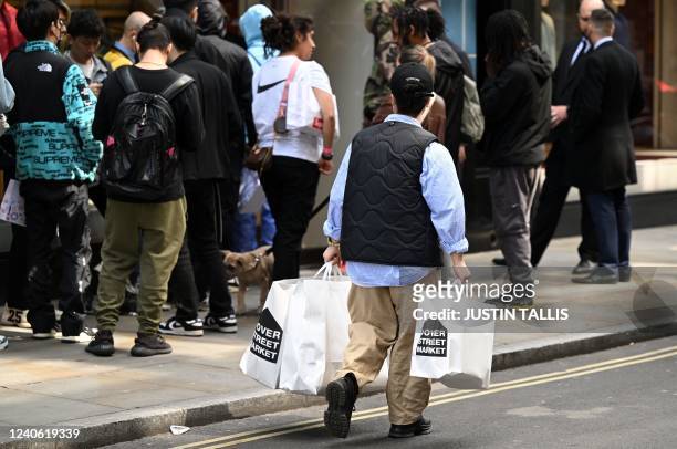 Man carries shopping bags past people queing to enter a shop in London on May 12, 2022. - Britain's economy shrank in March on fallout from soaring...