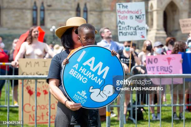 Pro-life protester holding a child holds a sign in front of counter-protesters during the National March for Life in Ottawa, Ontario, on May 12,...