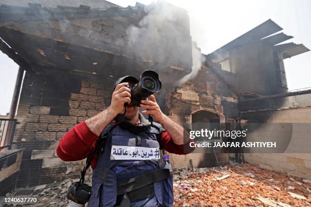 Reporter wearing a flak jacket with the hashtag in Arabic, "#Shireen Abu Akleh" takes a picture inside a house that was burnt during an Israeli...