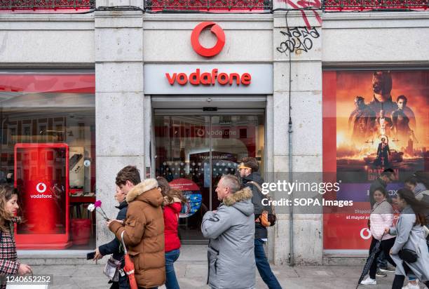 Pedestrians walk past the British multinational telecommunications corporation and phone operator Vodafone store.