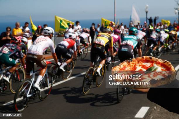 Spectator holds a Neapolitan pizza as riders compete during the 8th stage of the Giro d'Italia 2022, 153 kilometers between Napoli and Napoli,...