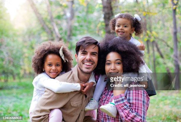 portrait of parents giving children piggybacks - multiracial person stock pictures, royalty-free photos & images